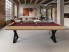 Billard Cross en chene nature liseret noir et tapis wine dans un loft en brique avec tableaux rouges et canape beige