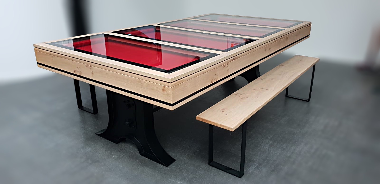 Quatre éléments de plateau en verre manipulables seul divulguent le tapis rouge de ce billard Atelier en bois teinté selon l'échantillon du client de la marque de billard Eurobillards et avec piétement en métal noir comme les deux bancs Fabrik qui l'accompagnent