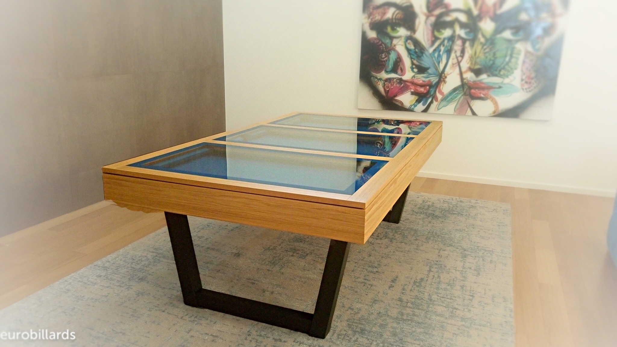 HARMONY-V en chêne naturel de la marque de biilard Eurobillards, ici converti en table par l'ajout d'un plateau BV de verre qui laisse apparaitre le tissu tournament dont le bleu fait écho avec le tableau sur lequel les ombres des visages rappellent les pieds en V. Chouette installation de notre meuble design chez ce client. Merci