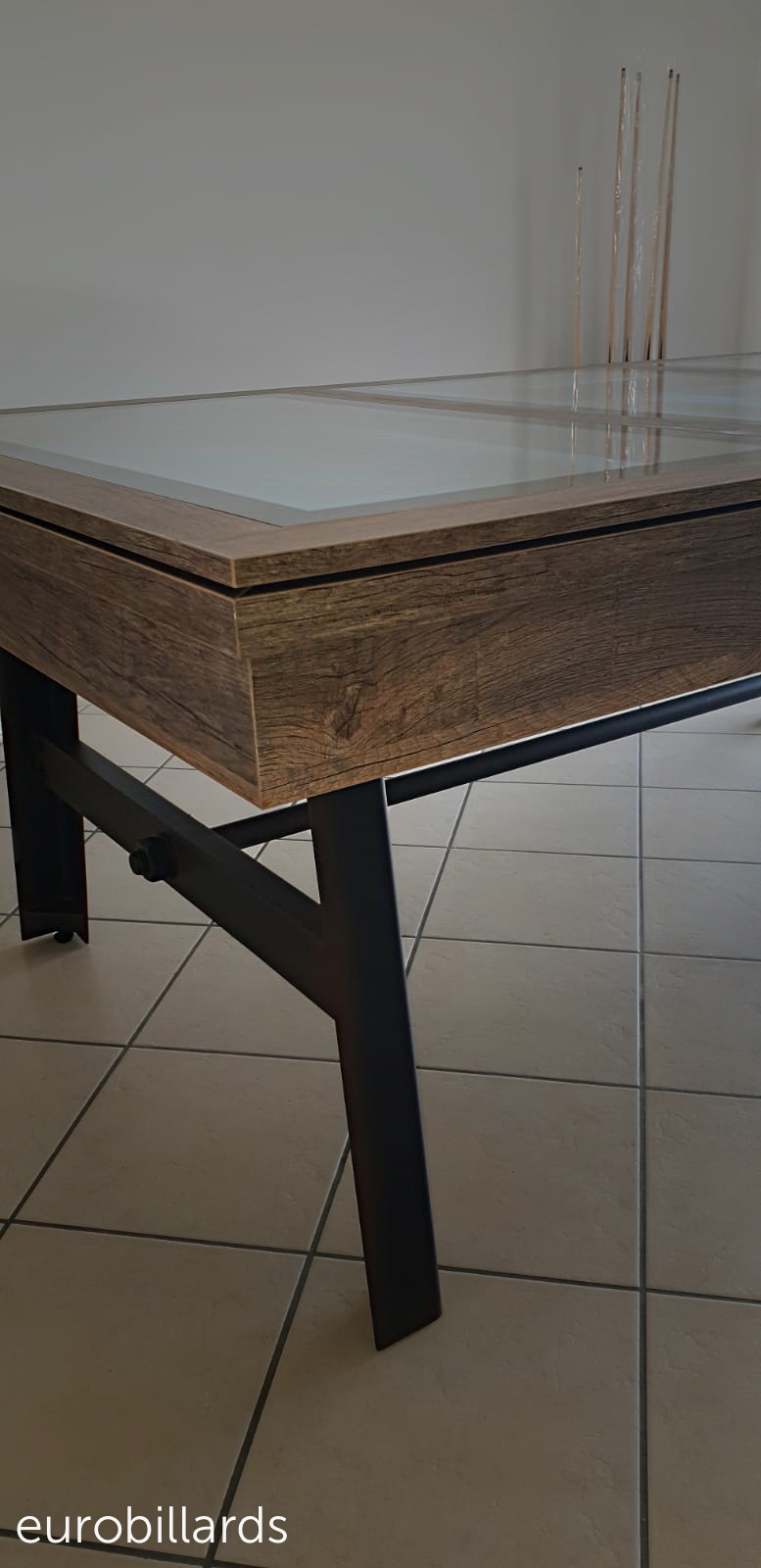 Plan rapproché sur l'angle du biilard convertible en table Vintage dont les pieds de métal reliés par une grande tige, boulons et fer plat contrastent agréablement avec le tissu bleu pétrole du jeu américain qui transparait sous le plateau BV à 3 verres Plan rapproché sur l'angle du biilard convertible en table Vintage dont les pieds de métal reliés par une grande tige, boulons et fer plat contrastent agréablement avec le tissu bleu pétrole du jeu américain qui transparait sous le plateau BV à 3 verres