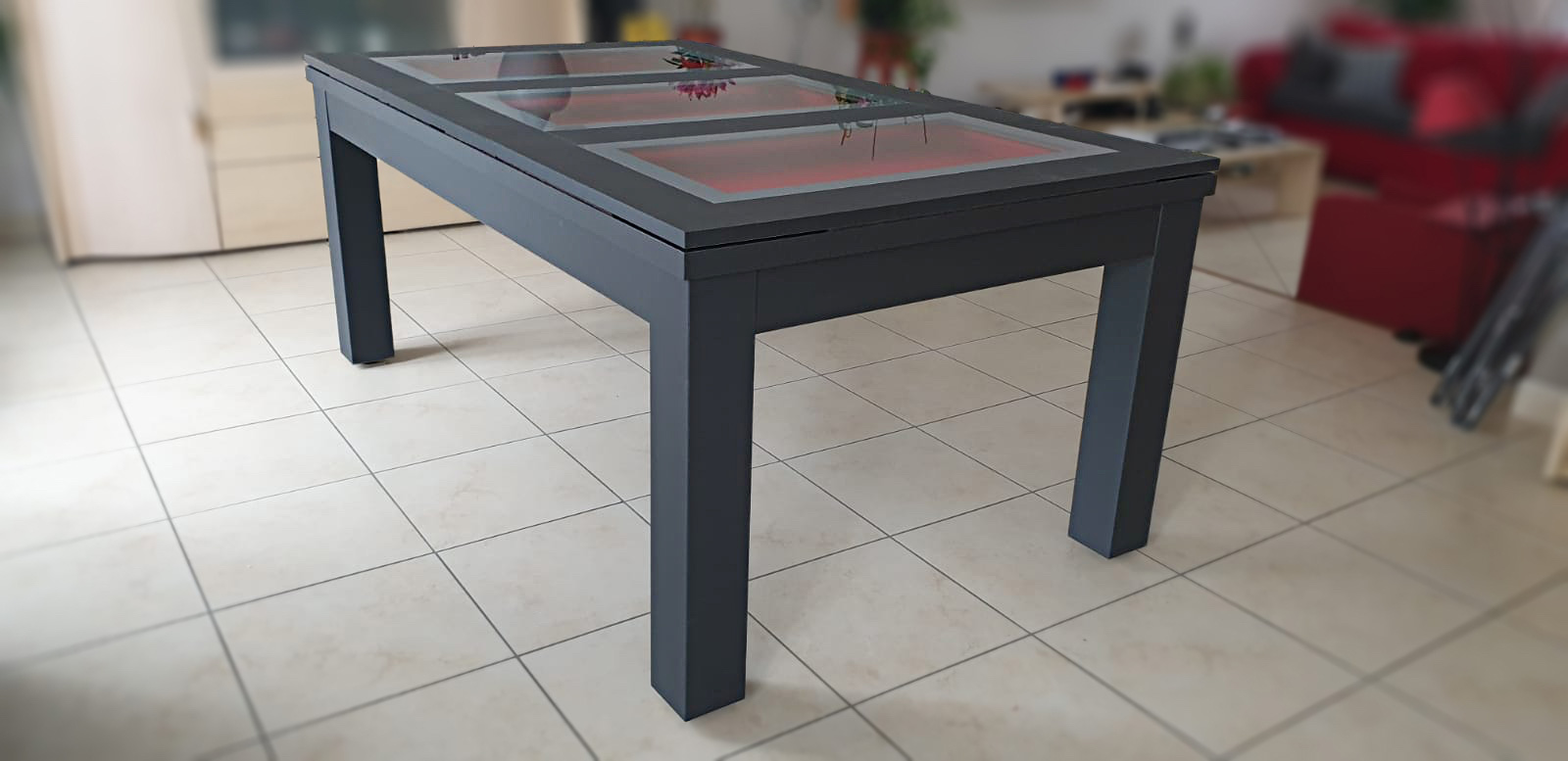 Dans une atmosphère crème et rouge ce billard moderne Trendy au tissu rouge se transforme en table à manger en verre dont le plateau est constitué de 3 encadrements au liseré gris clair