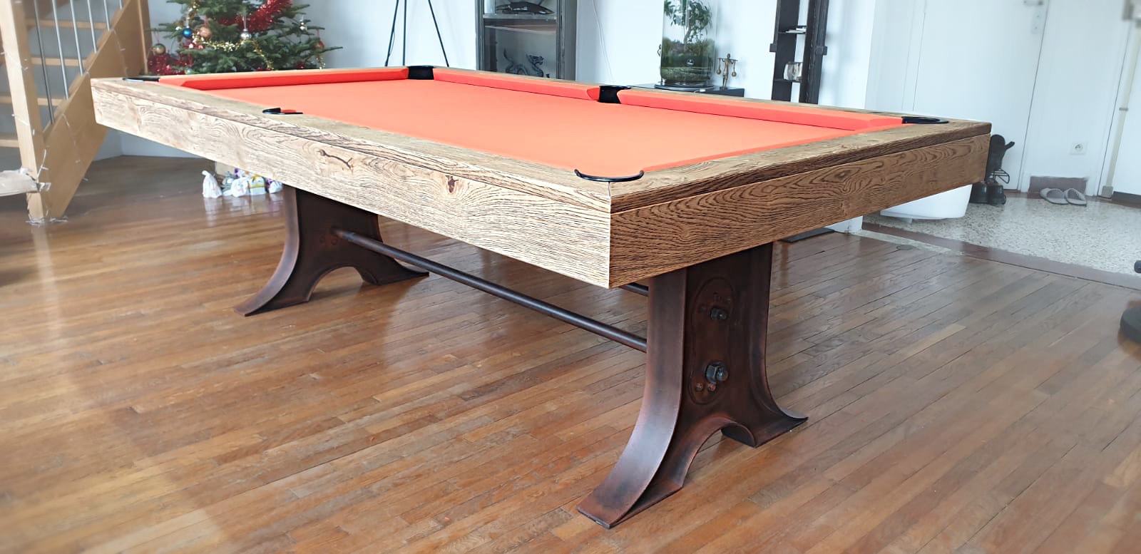 Le tissu de jeu orange fait ressortir les nuances de lumières des pieds tulipe en métal finition rouille. L'ensemble bicolore renforce l'aspect industriel de billard ATELIER transformable en table.