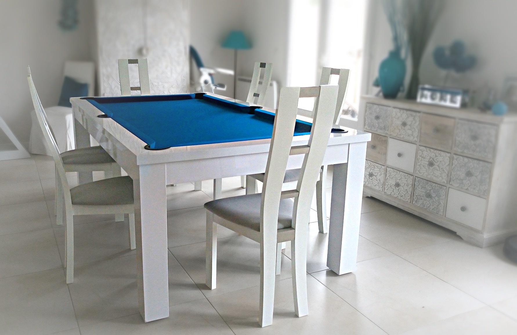 Le billard trendy blanc polaire brillant avec tissu bleu pétrole renforce le caractère de cette pièce de vie au buffet nuances de gris et aux accessoires turquoise posés sur le carrelage blanc