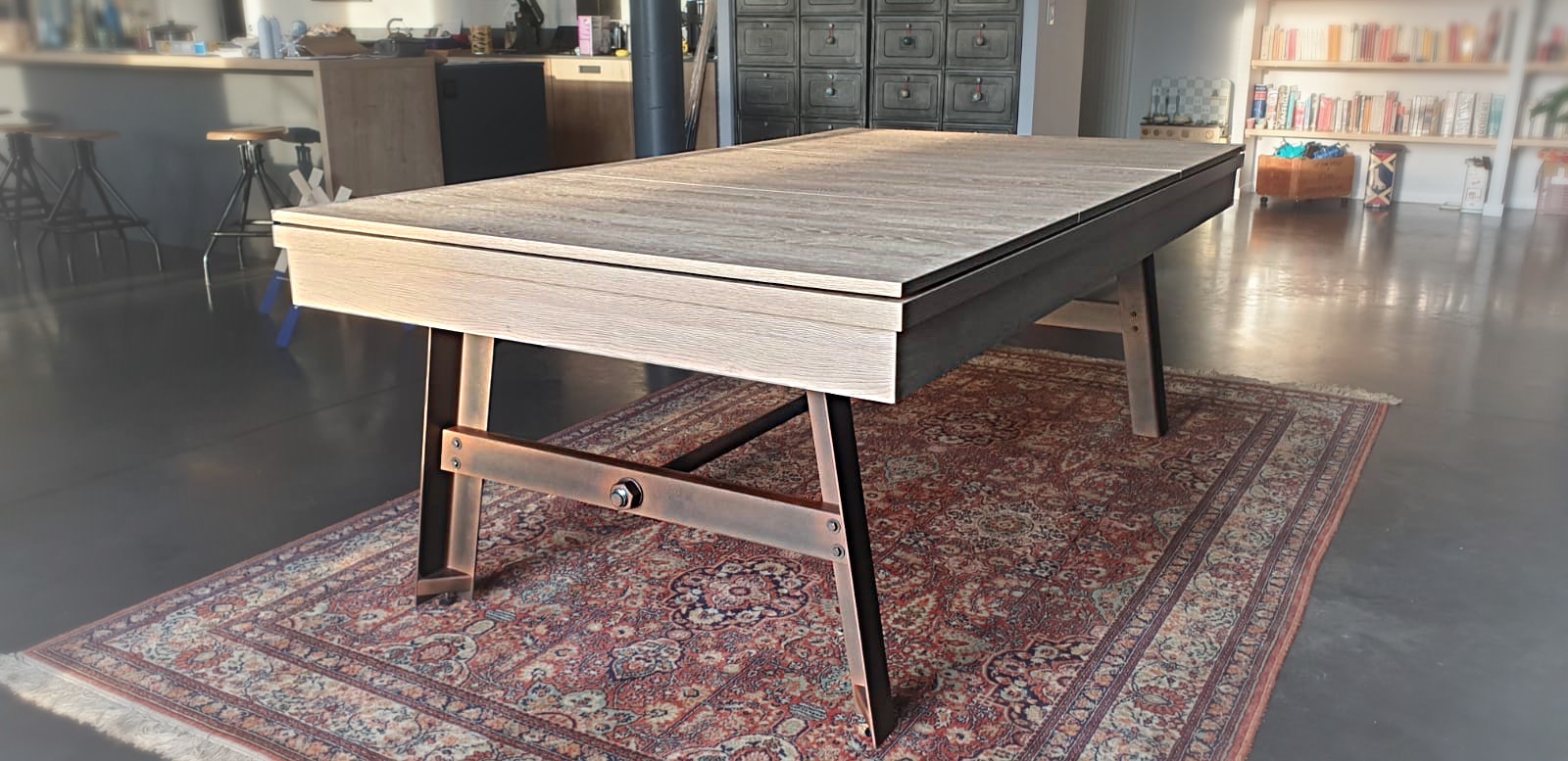 Dans son intérieur de charme au goût intemporel, notre client a installé ce billard table VINTAGE finition chêne nature avec ses pieds acier vieilli façon rouille et son plateau ST sous la lumière du jour qui met à l'honneur le travail soigné des ouvriers de notre marque de billard pourtant pas cher. L'ensemble s'accorde harmonieusement tant avec le tapis oriental que les tabourets à vis sur le sol en béton ciré